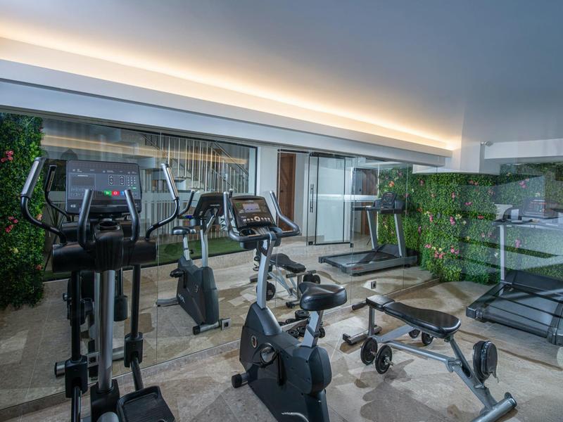 Attrezzature da palestra moderne in una sala fitness luminosa e ariosa con pareti di vetro e piante.