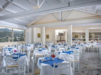 Ampia sala da pranzo luminosa con tavoli bianchi, tovaglie blu e vista sulle colline verdi.