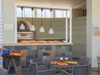 Accogliente area esterna con sedie, tavoli, birra e snack davanti a un bar con prodotti da forno.