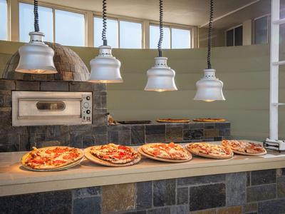 Diverse pizze appena sfornate su un bancone di pietra davanti a un forno tradizionale per pizza.