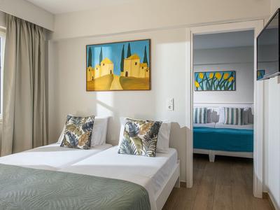 Camera d'hotel moderna con letto, cuscini colorati e arte astratta sulle pareti.