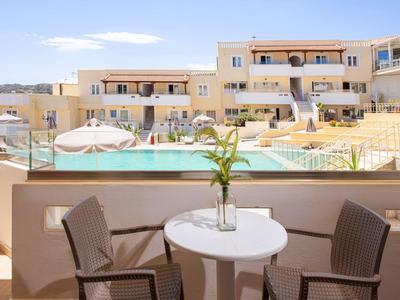 Vista da un balcone con tavolo e sedie che si affaccia su una piscina e un edificio dell'hotel sotto un cielo limpido.