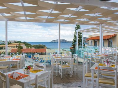 Ristorante con tavoli e sedie bianchi, coperto con vista sul mare e isola sullo sfondo.