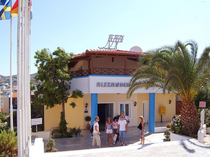 Entrée d'un hôtel peint en jaune avec des portes bleues et plusieurs personnes devant.