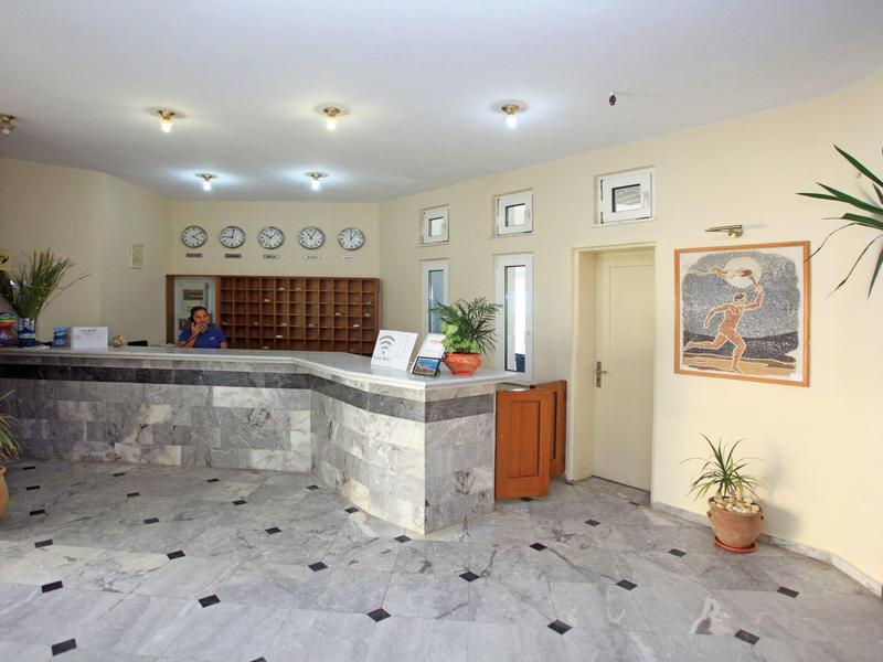 Hall d'hôtel lumineux avec réception en marbre, personnel multilingue et plantes décoratives.