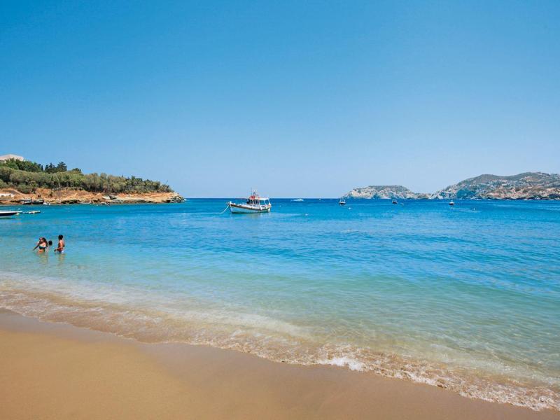 Plage de sable avec eau bleue claire, personnes dans la mer et bateau sous ciel dégagé