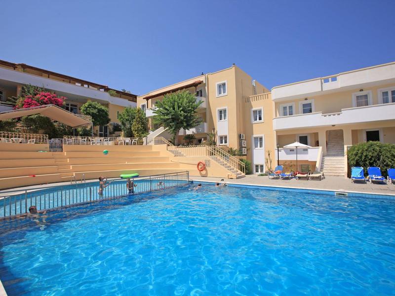 Hôtel avec grande piscine extérieure, terrasse ensoleillée et bâtiments à plusieurs étages sous un ciel bleu clair.