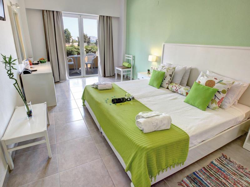 Chambre d'hôtel moderne avec lit double, couvre-lit vert et balcon avec vue.