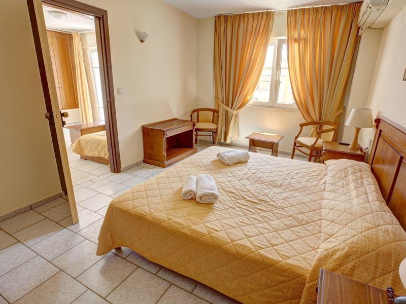 Chambre d'hôtel confortable avec lit double, deux chaises et fenêtre avec rideaux dorés.