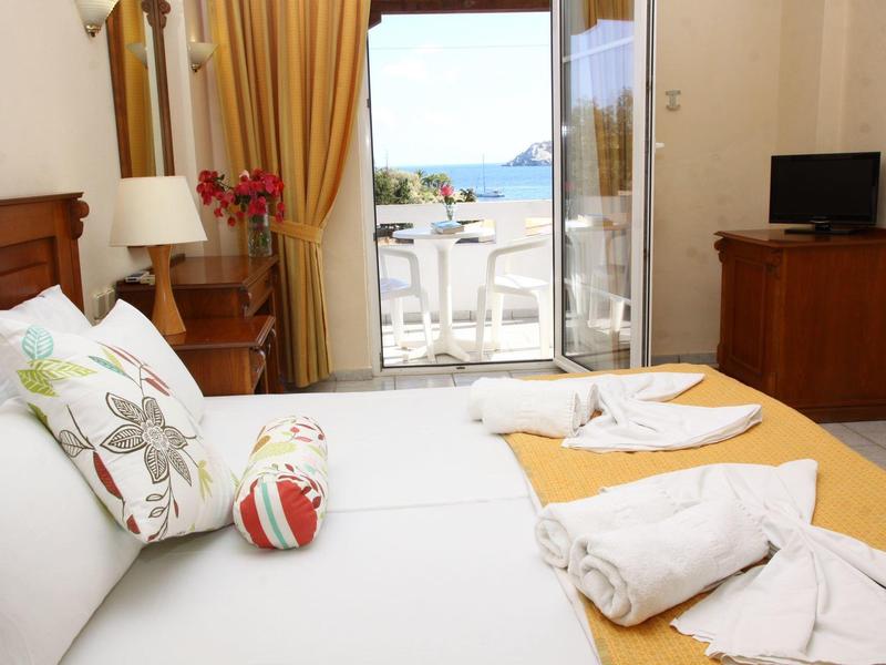 Chambre d'hôtel avec lit double, balcon avec vue sur la mer, télévision et rideaux jaunes.
