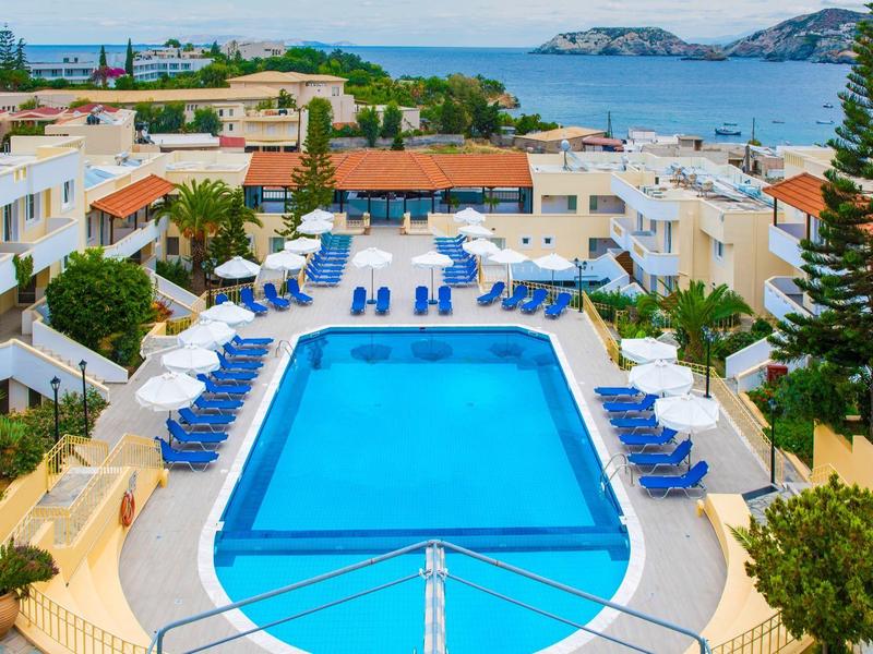 Piscine d'hôtel avec chaises longues bleues et vue sur la mer et les bâtiments environnants.