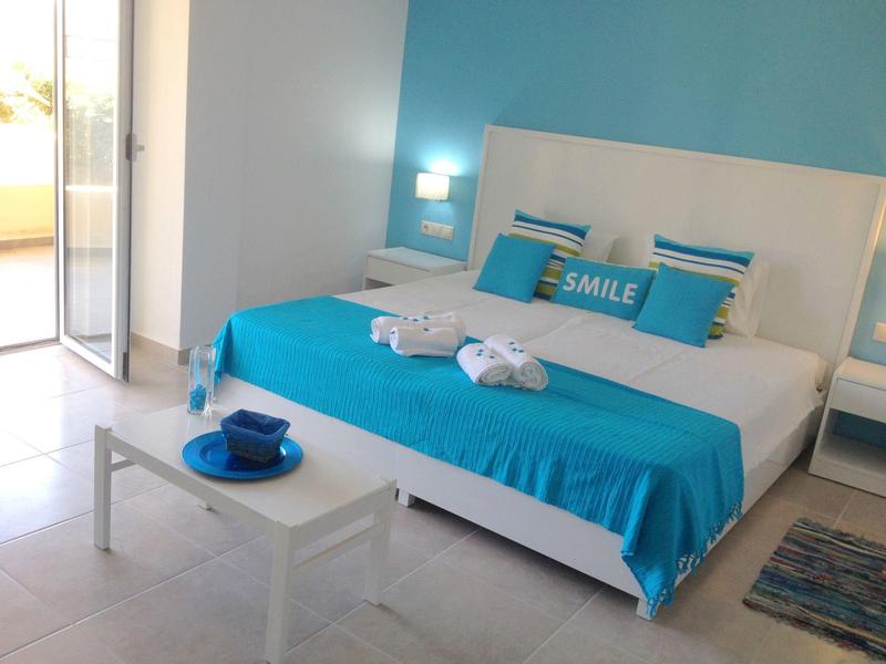 Chambre d'hôtel lumineuse avec lit double, literie bleu et blanc, et accès au balcon.