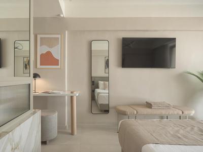 Habitación de hotel moderna con cama, espejo de pared, televisor y decoración minimalista en tonos neutros.