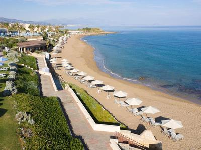 Spiaggia con ombrelloni bianchi, mare calmo, vista di passeggiata e aree verdi.