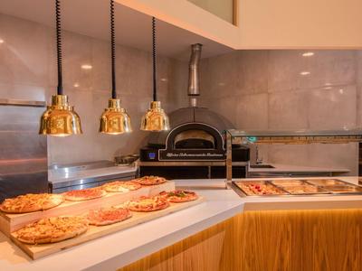 Interior de una pizzería con horno de leña y pizzas en el mostrador bajo lámparas doradas.