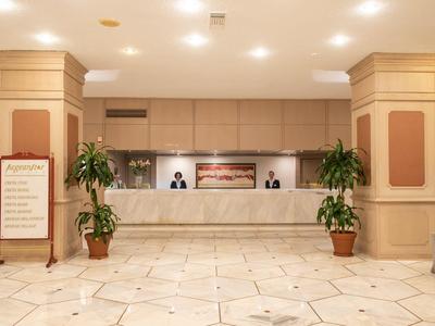 Lichte hotelreceptie met marmeren vloer, balie en potplanten aan beide zijden.