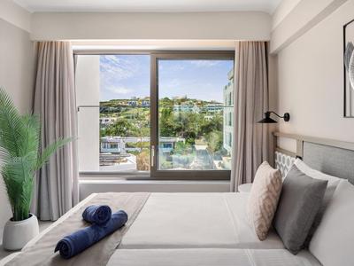 Helles Schlafzimmer mit großem Fenster, Blick auf Landschaft und Pool im Hotel.