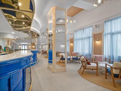 Moderne hotel-loungesectie met blauwe bar, witte muren en gezellige zitgroepen bij daglicht.