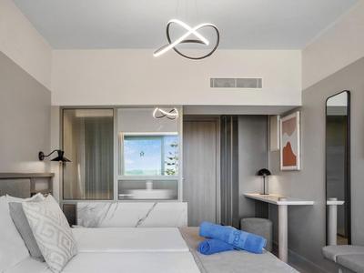 Modernes Hotelzimmer mit Doppelbett, Schreibtisch und blauem Handtuch auf weißer Bettdecke.