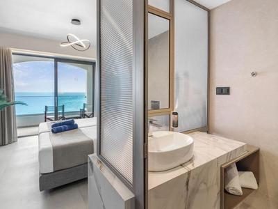 Modernes Hotelzimmer mit Blick aufs Meer, hellem Interieur und offenem Badezimmerbereich.