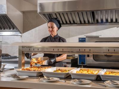 Een chef-kok serveert warme gerechten in een moderne hotelkeuken.
