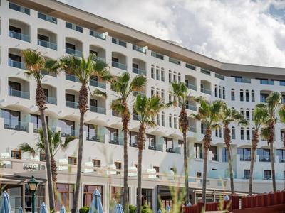 Meerlaag hotel met balkons en palmbomen ervoor onder een bewolkte hemel.