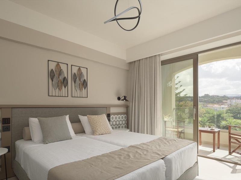 Habitación de hotel luminosa con dos camas, muebles modernos y balcón con vista a áreas verdes.