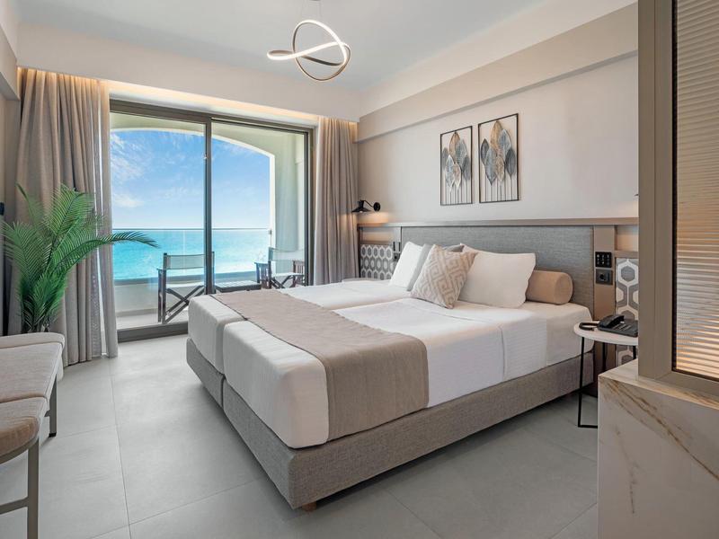 Moderna habitación de hotel con cama doble, balcón y vista al mar en clima despejado.