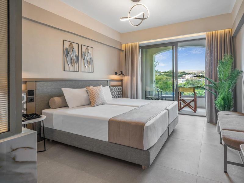 Habitación de hotel moderna con cama doble grande y balcón con asiento y vista a la naturaleza.