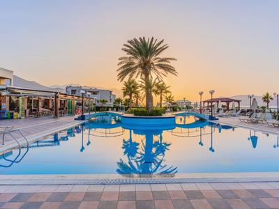 Großer Pool mit Palmeninsel, umliegenden Liegen und Gebäuden, im Sonnenunterganglicht.