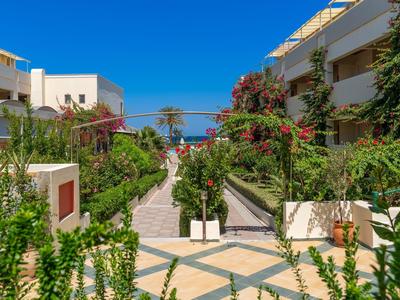 Moderner Innenhof mit bunten Blumen, grünen Pflanzen, weißen Gebäuden und blauem Himmel.