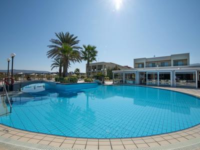 Rond buitenzwembad met blauw water, palmboom en aangrenzend wit gebouw bij zonlicht.