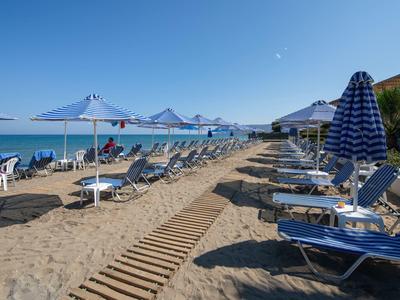 Sandstrand mit blauen Liegestühlen, weißen Sonnenschirmen und blauem Himmel am Meer.