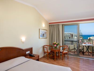 Modern hotelkamer met tweepersoonsbed, kleine tafel en zeezicht vanaf balkon.