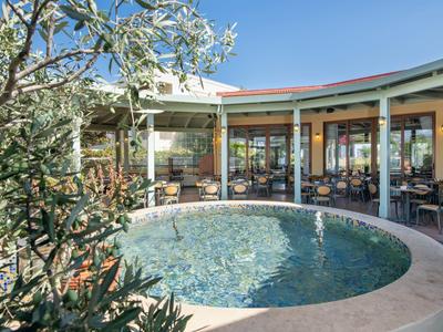 Rond zwembad voor een hotelrestaurant met buitentafels bij zonnig weer.