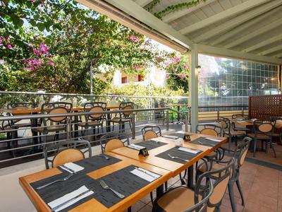 Overdekt terras met tafels en stoelen omringd door groene planten en bloemen.