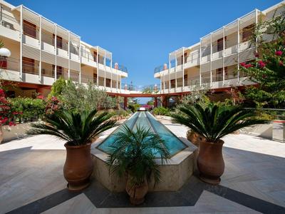 Binnenplaats van een hotel met zwembad en grote bloempotten bij heldere lucht.