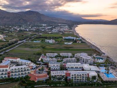 Große Hotelanlage mit mehreren Gebäuden, Pools und Meer an bewölktem Abendhimmel.