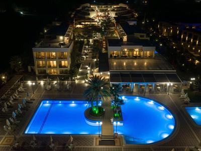 Nachtzicht op een verlicht hotel met een groot blauw zwembad en omliggende zitgedeeltes.