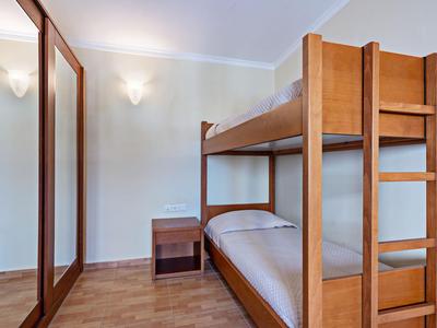 Houten stapelbed en nachtkastje in een eenvoudige hotelkamer met parketvloer.