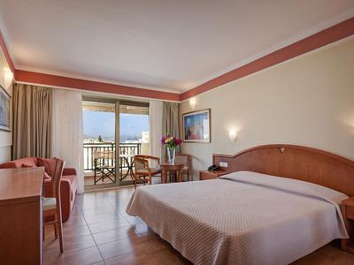 Lichte hotelkamer met groot bed en balkon met uitzicht op zee.