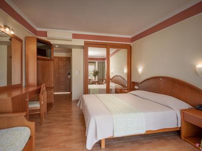 Lichte hotelkamer met tweepersoonsbed, houten meubels en spiegels aan de muur.