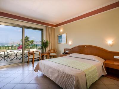 Lichte hotelkamer met tweepersoonsbed, balkon en uitzicht op zee.
