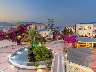 Hotelterras met bloemen, palmbomen en uitzicht op gebouwen bij zonsondergang.