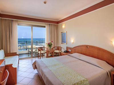 Lichte hotelkamer met tweepersoonsbed, bureau en balkon met uitzicht op zee.