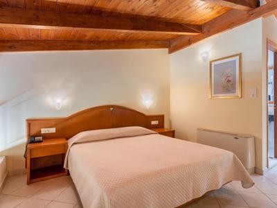 Gezellige hotelkamer met houten balkenplafond, tweepersoonsbed en nachtkastje onder schuine plafond.