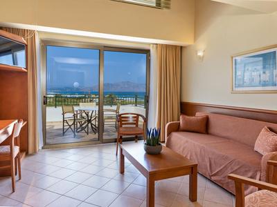 Knus hotelkamer met bank, tafel en balkon met uitzicht op zee.