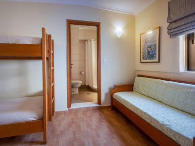 Kleine hotelkamer met stapelbed, bank, houten vloer en open badkamerdeur.
