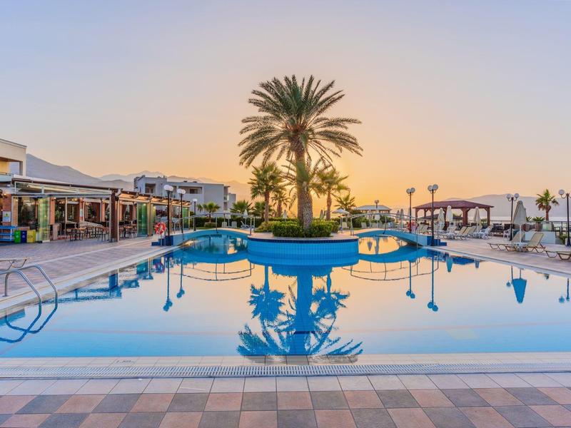 Großer Pool mit Palmeninsel, umliegenden Liegen und Gebäuden, im Sonnenunterganglicht.