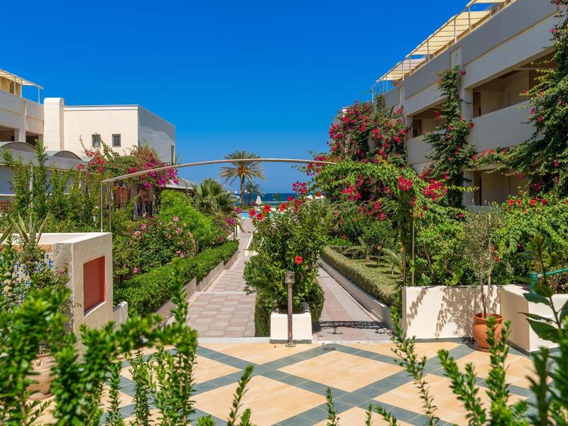 Moderner Innenhof mit bunten Blumen, grünen Pflanzen, weißen Gebäuden und blauem Himmel.